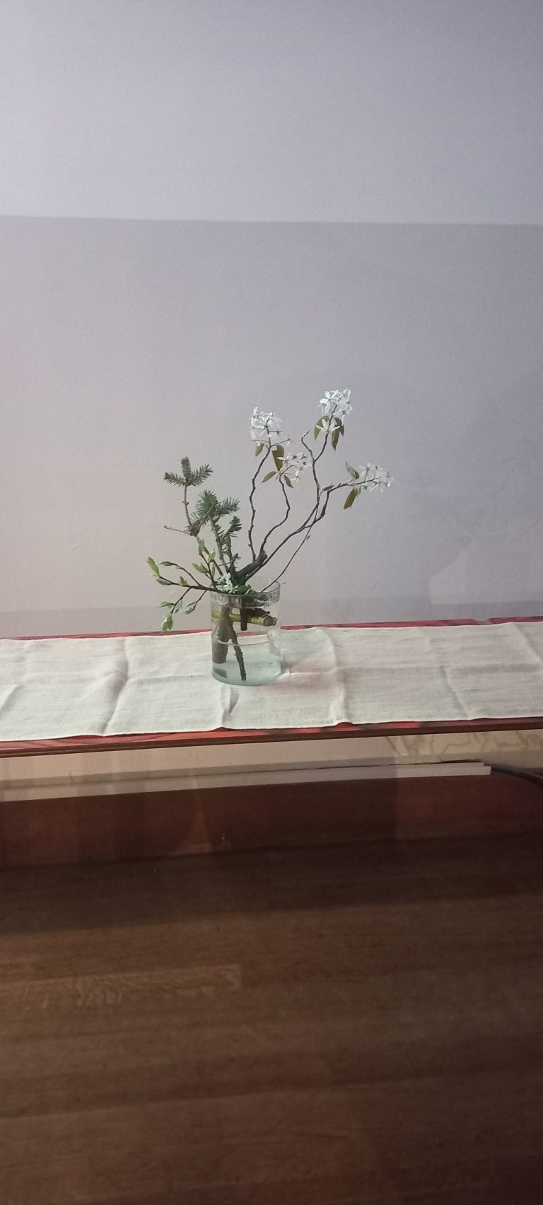A table set with a white runner and a small vase of white flowers