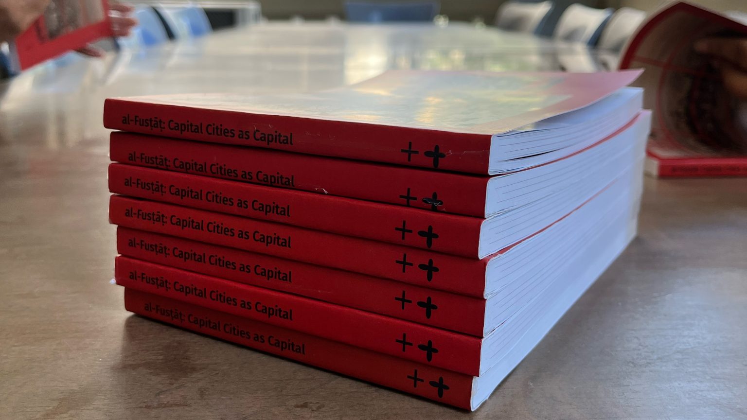 A stack of copies of the red book al-Fustat: Capital Cities as Capital on a wooden table