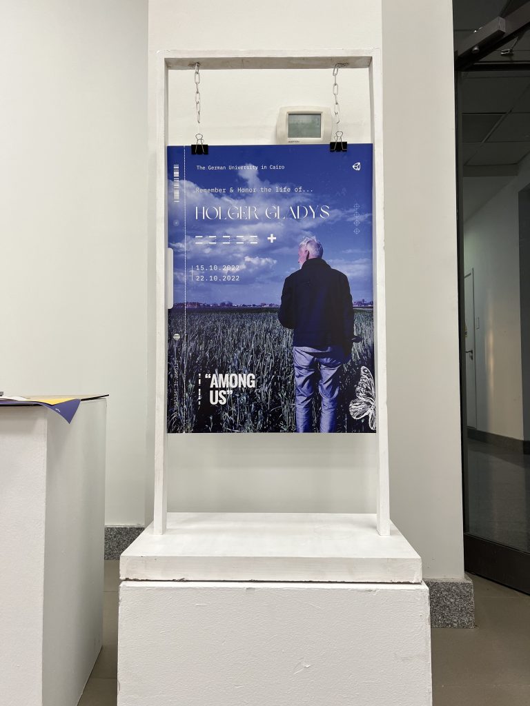 Entrance to the Among Us memorial exhibition: a large portrait of Holger Gladys on a white display stand