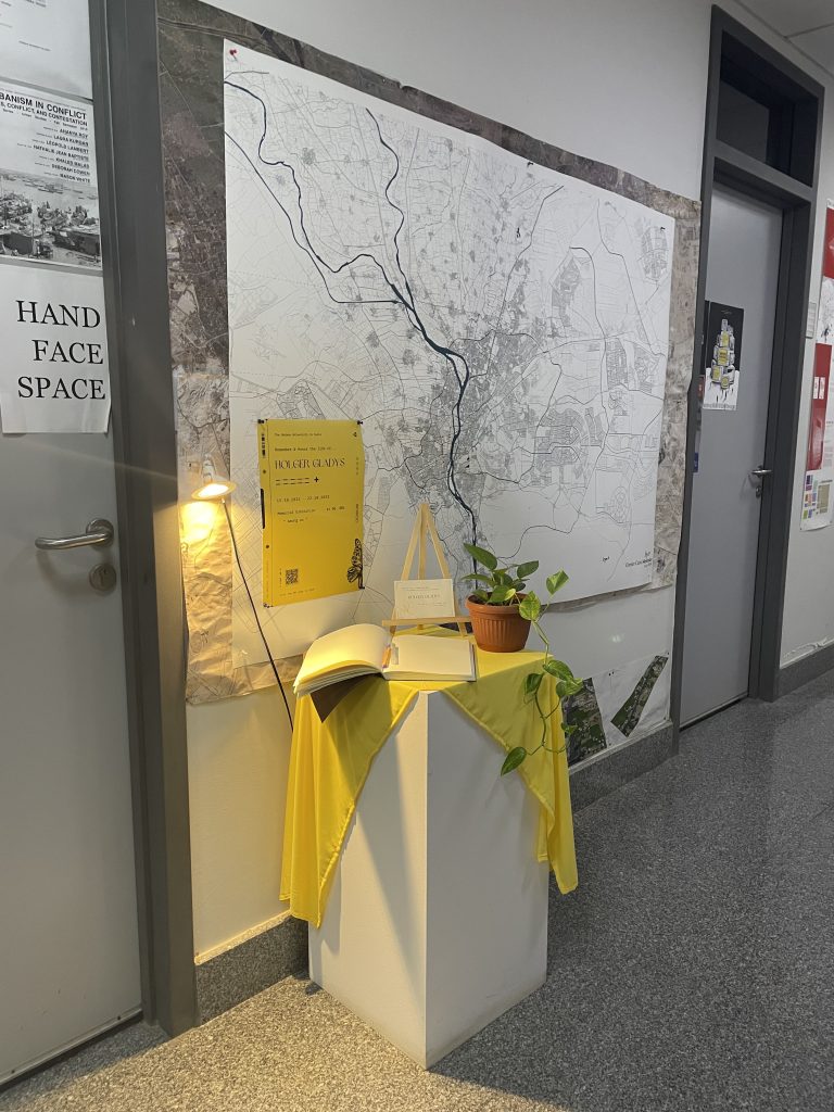 A large map on the gallery wall beside a plinth draped in yellow fabric at the Among Us exhibition