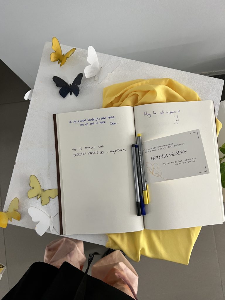 An open guestbook and pen on yellow fabric, surrounded by folded paper butterflies