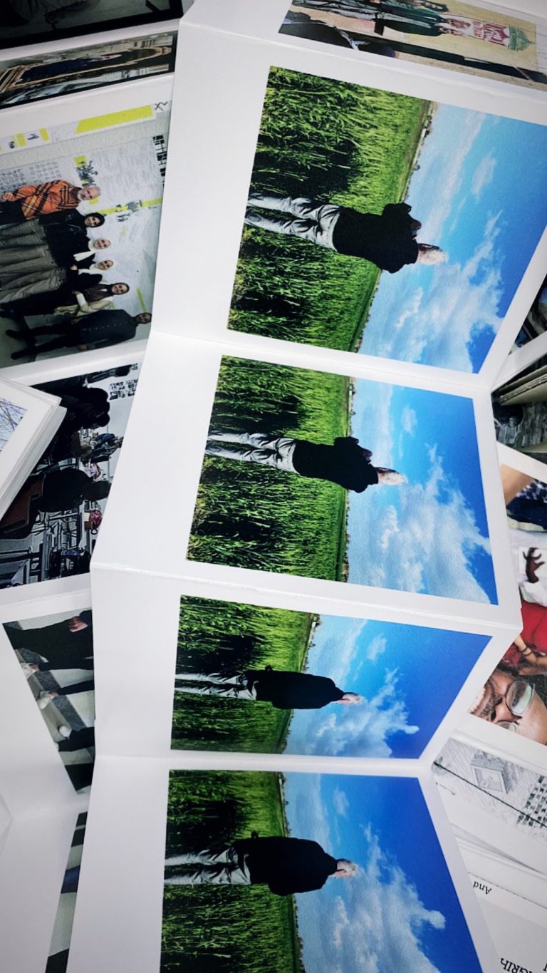 A long folded strip of printed photographs hanging on display at the Among Us exhibition