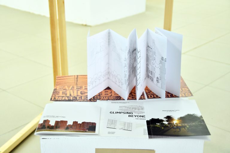 A folded concertina booklet of drawings displayed on a table with printed cards